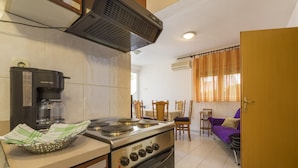 A compact kitchen with a coffee maker, stove, oven, and a dining area with a table and chairs. - Apartments Vilma (Crikvenica)