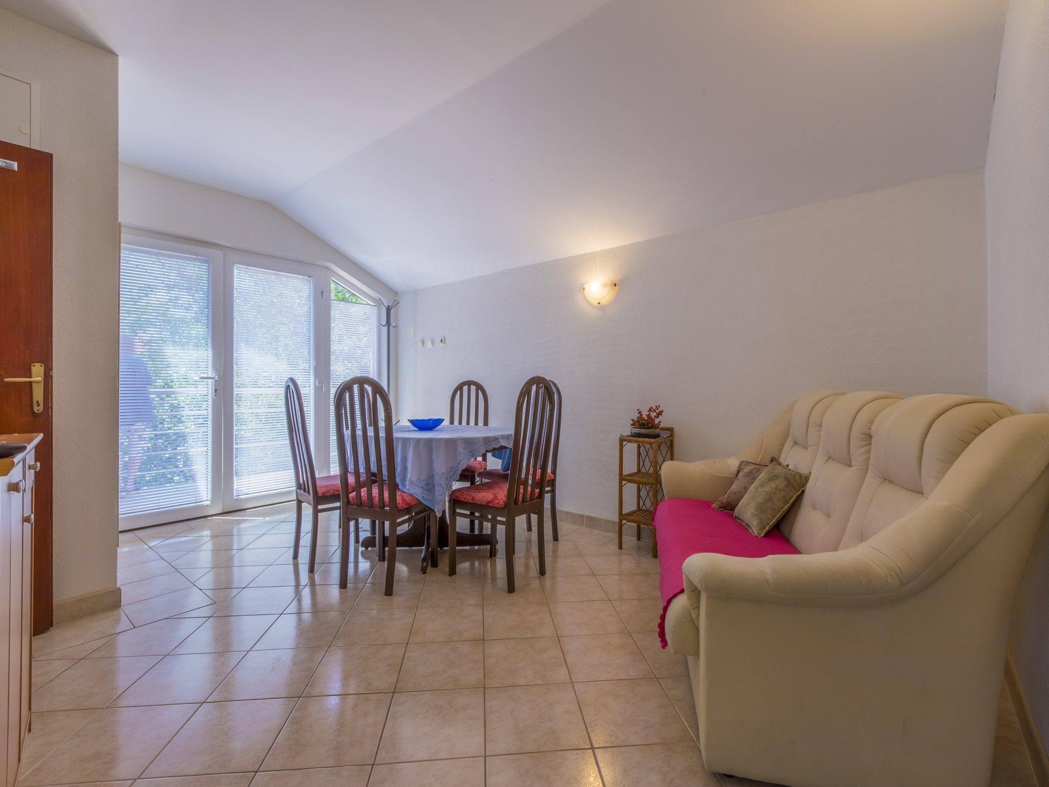A dining area with a table and chairs, a sofa, and a window with blinds.