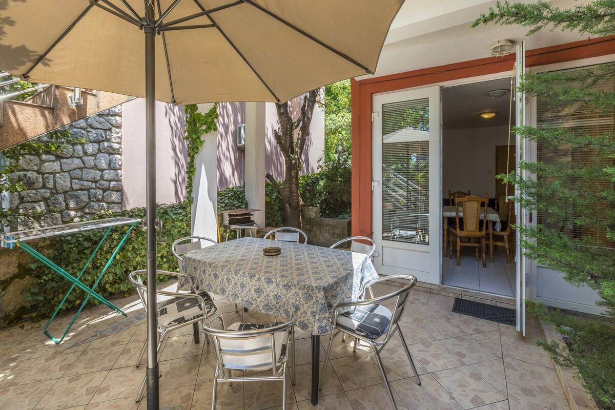 A patio with a table and chairs, a large umbrella, and a stone wall.