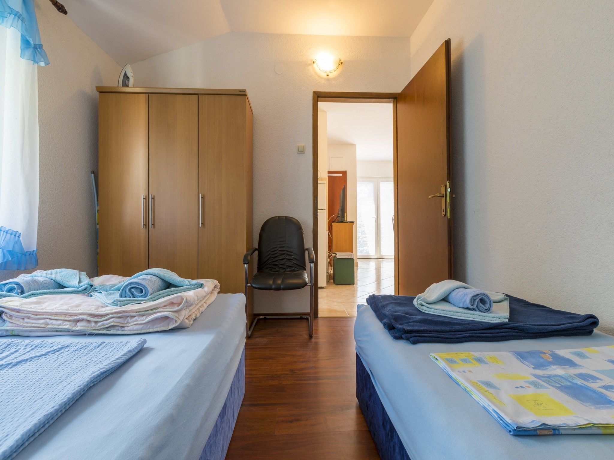 A bedroom with two beds, a chair, and a wardrobe.