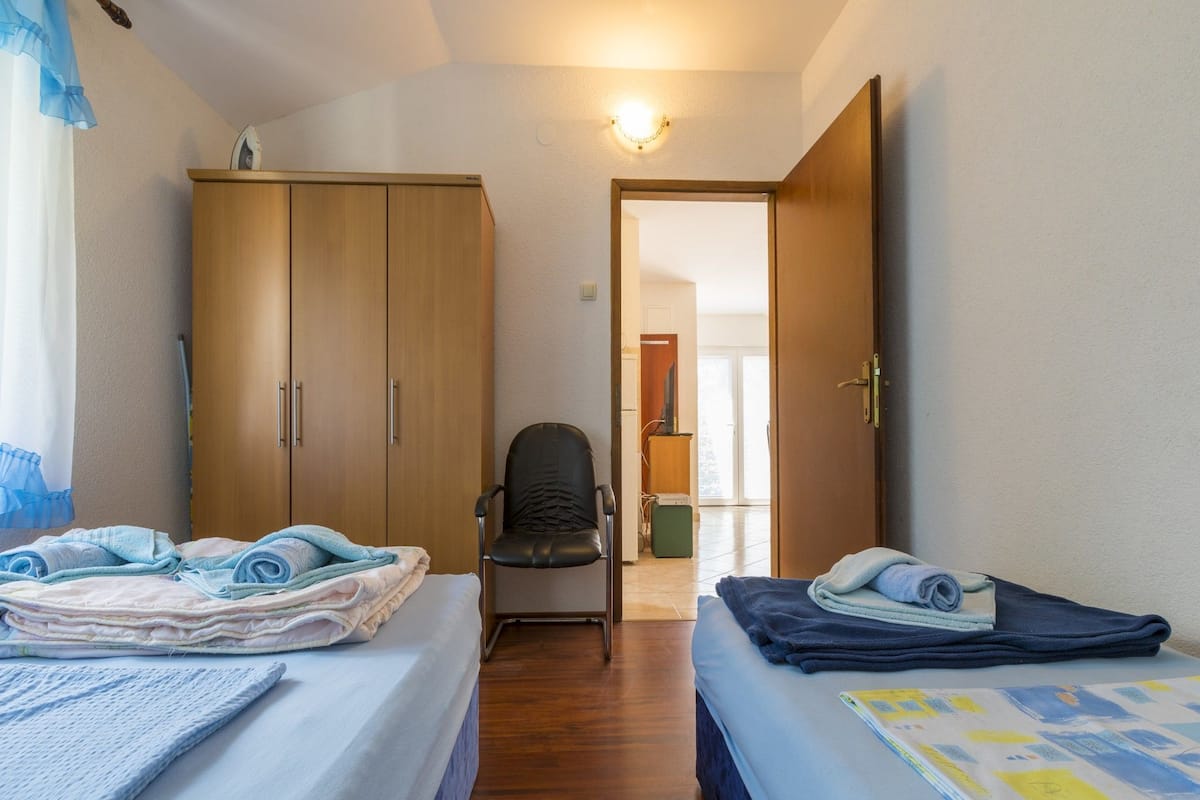 A bedroom with two beds, a chair, and a wardrobe.