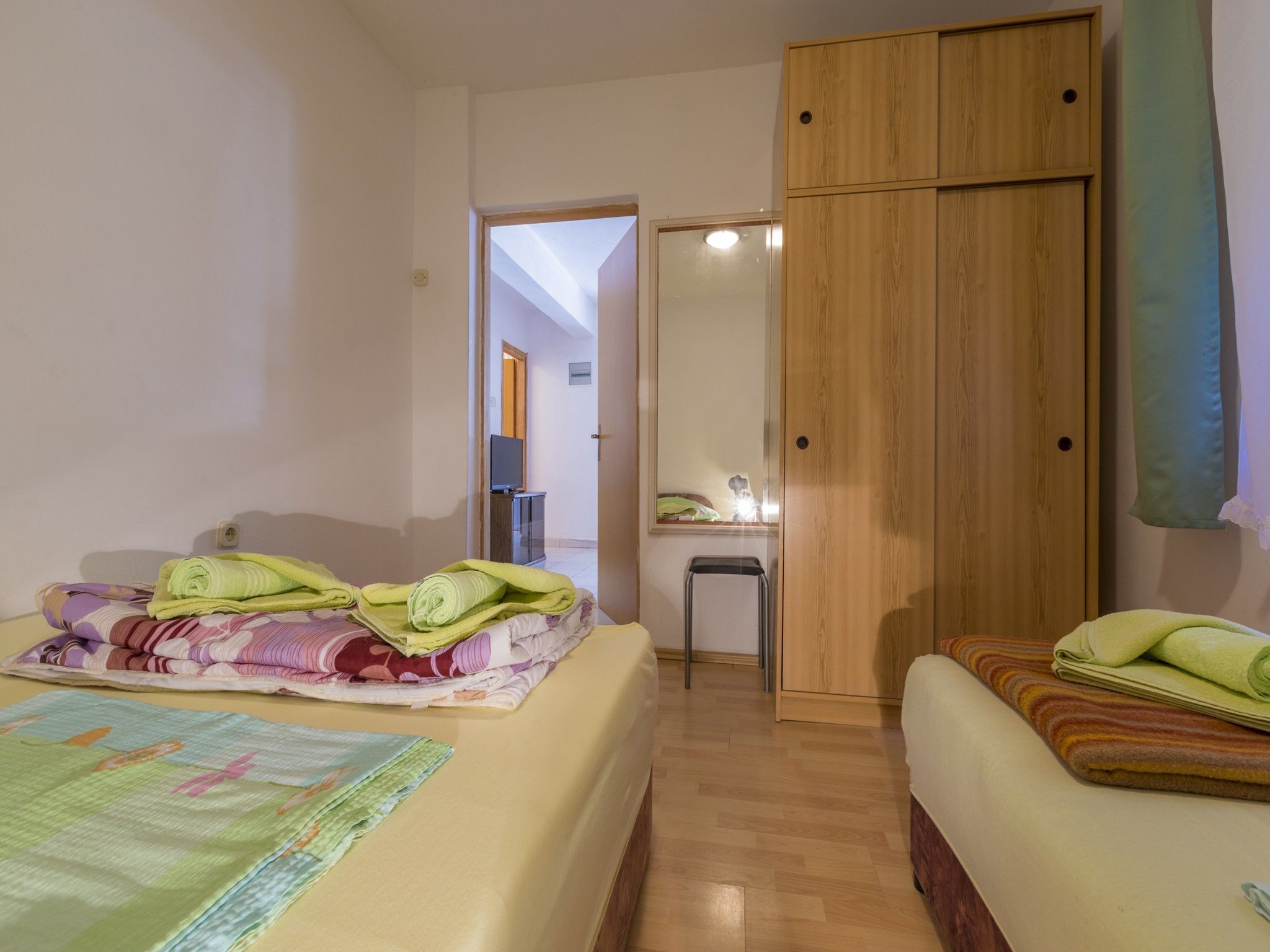 A hotel room with two beds, a wooden wardrobe, a small desk, and a mirror.