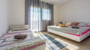 A bedroom with two beds, a large window with curtains, a bedside table with a lamp, and a tray with orange juice. - Apartment Paula (Jadranovo)