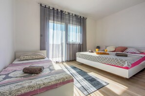 A bedroom with two beds, a window with curtains, a bedside table with a lamp, and a bedside tray with a bottle and glasses.