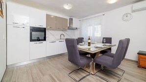 Een moderne keuken met witte kasten, een inbouwoven en een eethoek met een glazen tafel en vier stoelen.