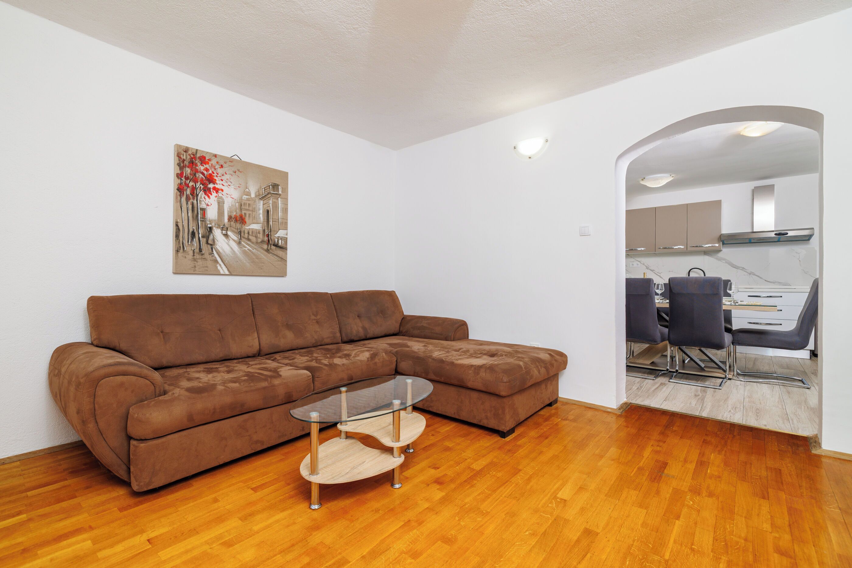 A living room with a brown sectional sofa, a glass coffee table, and a painting on the wall.