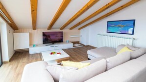 Ein modernes Wohnzimmer mit Holzboden, einem Flachbildfernseher, einem weißen Sofa und einem Couchtisch mit Früchten.