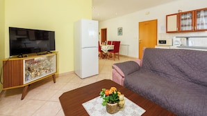 A living room with a television, a refrigerator, a sofa, and a dining area in the background.