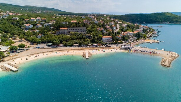 An aerial view of a coastal town with a beach, clear blue waters, and a mix of residential and commercial buildings. - Apartment Blazic (Jadranovo)