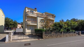 A two-story residential building with a stone wall and metal gate, featuring balconies and a clear blue sky. - Apartment Blazic (Jadranovo)