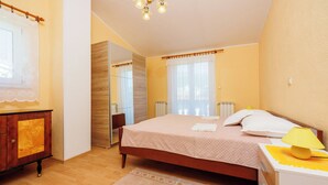 A bedroom with a bed, bedside table, lamp, and a wooden dresser. - Apartment Blazic (Jadranovo)