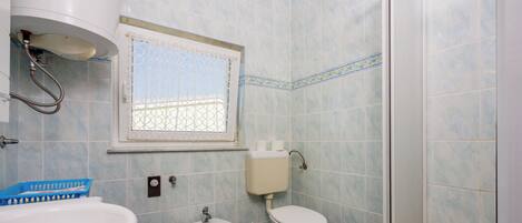 Un baño con bidé, inodoro, lavamanos y una ventana con una celosía decorativa.