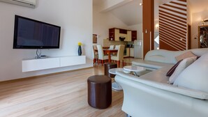 A modern living room with a flat-screen TV, a sofa, a coffee table, and a dining area in the background. - Apartments Barbara 2 (Jadranovo)