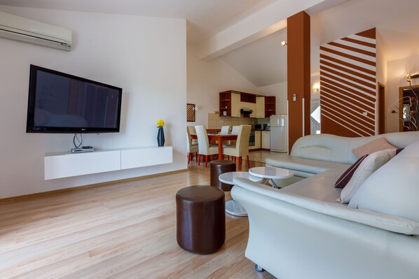 A modern living room with a flat-screen TV, a sofa, a coffee table, and a dining area in the background.