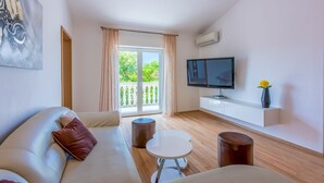 A modern living room with a sofa, a small round table, and a TV mounted on the wall. - Apartments Barbara 2 (Jadranovo)