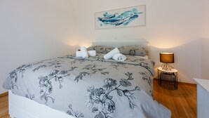 A neatly made bed with floral bedding, a wall-mounted abstract painting, and a bedside lamp. - Apartments Barbara 2 (Jadranovo)