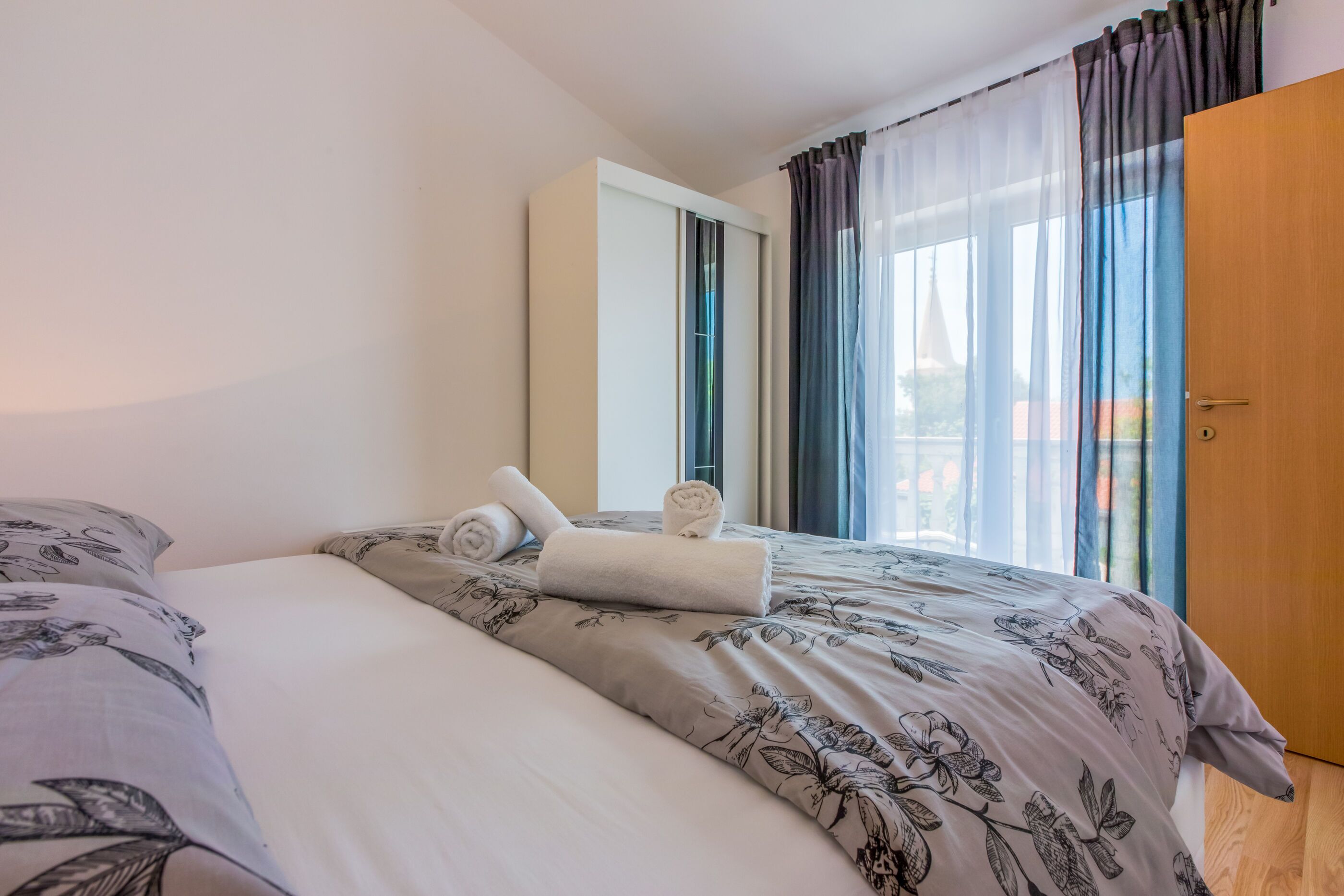 A hotel room with a bed, a wooden door, and a window with curtains.