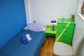 Ein kleines Schlafzimmer mit einem Einzelbett, einem grünen Schreibtisch mit Schubladen, einem Stuhl und einem Nachttisch mit Lampe.