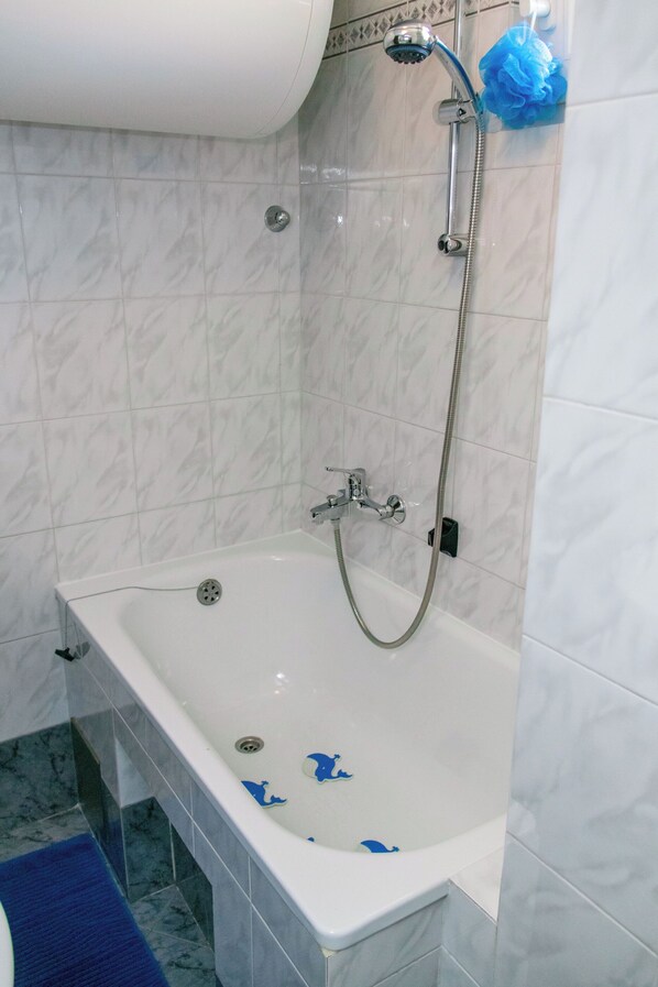 Ein Badezimmer mit einer weißen Badewanne, einer Duschbrause und einer blauen Badematte.