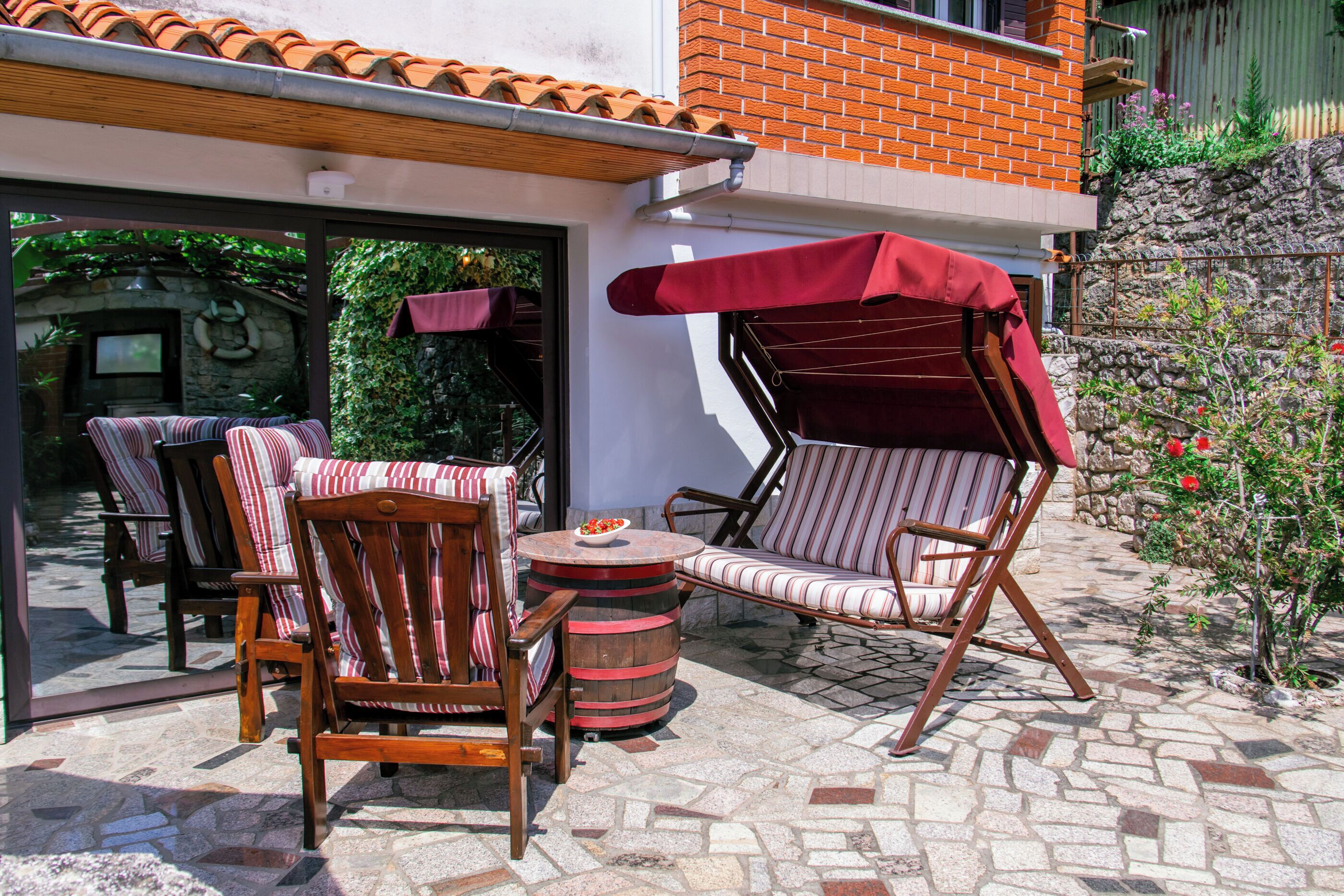Une terrasse extérieure avec deux chaises à rayures, une table ronde et un parasol rouge.