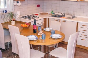 Ein Essbereich mit einem runden Tisch, Stühlen, einer Weinflasche, Gläsern und einer Obstschale.
