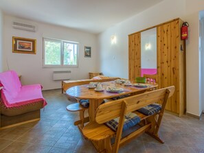 A cozy dining area with a wooden table and chairs, a pink chair, and a wooden cabinet with a fire extinguisher.