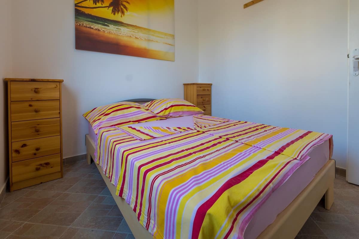 A bedroom with a bed, a wooden dresser, a nightstand, and a painting of a beach scene.