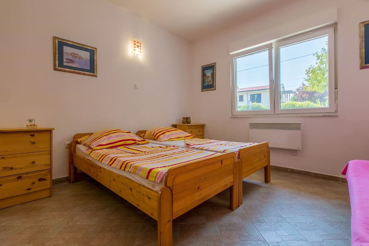 A bedroom with a wooden bed, a dresser, a nightstand, a window with a view, and two wall-mounted lights.
