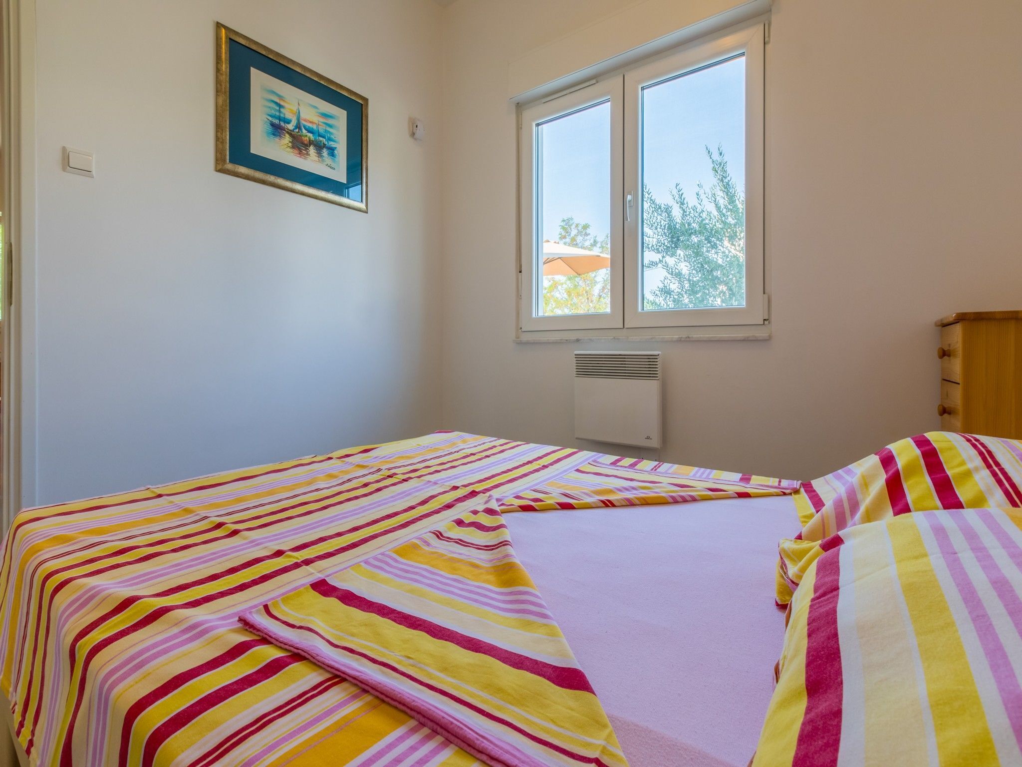 Una camera da letto con un letto, una finestra, un termosifone e un quadro appeso al muro.