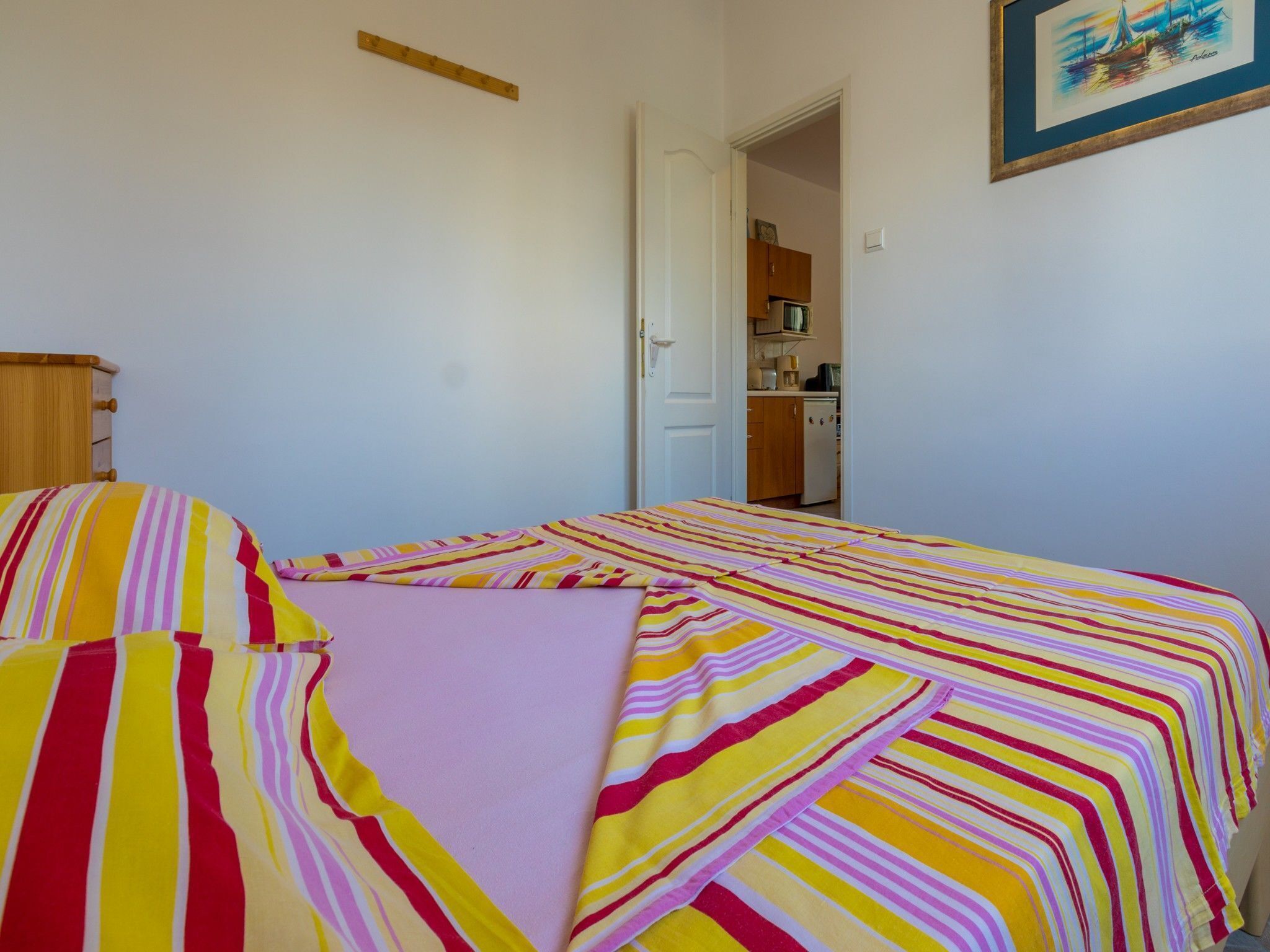 Un dormitorio con una cama cubierta con ropa de cama a rayas, un cabecero de madera y una puerta que da a una kitchenette.