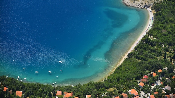 Vista aérea de una zona costera con playa, barcos y una pequeña isla.