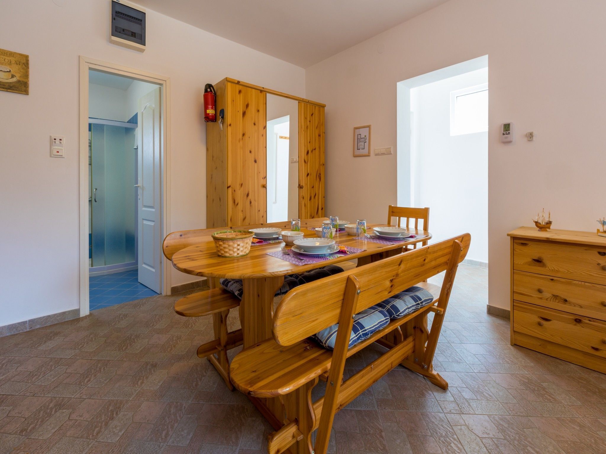 A dining area with a wooden table and benches, a wooden cabinet, and a door leading to a bathroom.