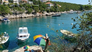 A coastal marina with boats docked, clear water, and houses on a hillside in the background. - Apartments Ljiljana (Dramalj)