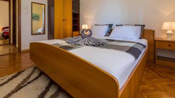 Una cama bien tendida con un alfombra a rayas, un armario de madera y una mesita de noche con una lámpara.