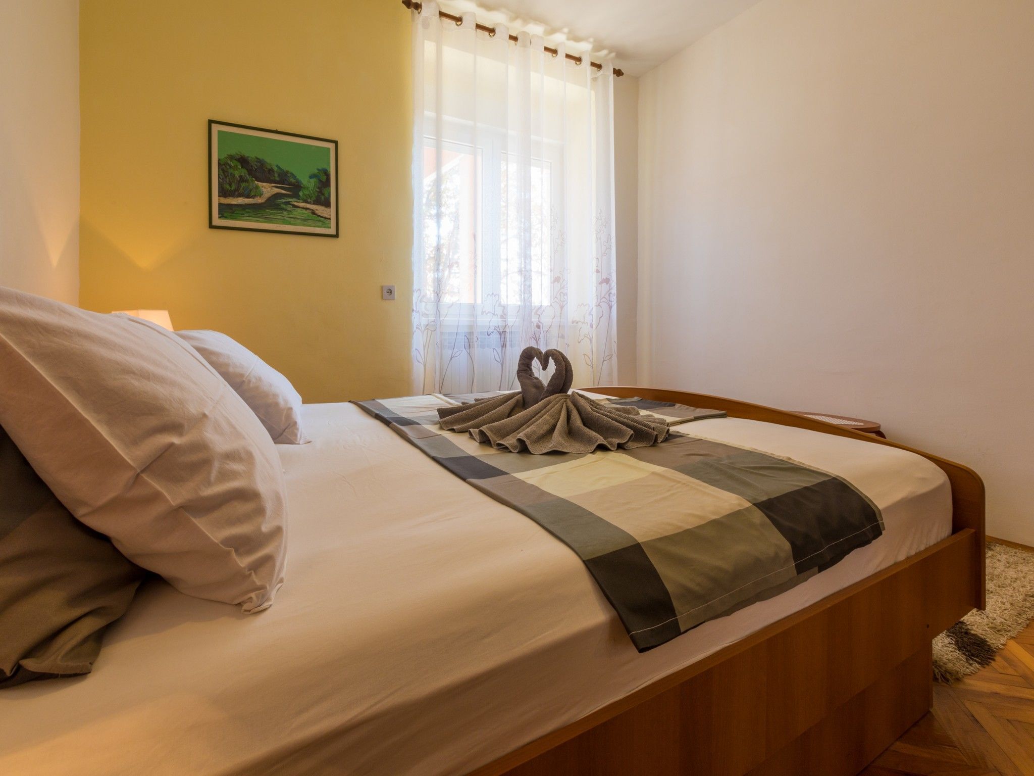 Una cama bien hecha con un edredón a cuadros, almohadas y una toalla dispuesta en forma de corazón.