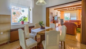 A dining area with a wooden table and chairs, a chandelier, and a view of the outdoors through large windows. - Apartments Ljiljana (Dramalj)
