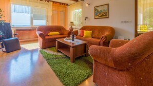 A cozy living room with a wooden ceiling, a sofa set, a coffee table, and a view of the outdoors through large windows. - Apartments Ljiljana (Dramalj)