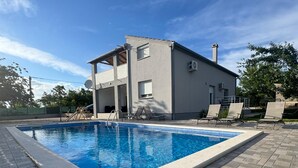 A swimming pool with a modern house in the background. - Apartment Cherry Garden (Zemunik Donji)