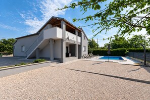 A modern two-story house with a covered outdoor area, a swimming pool, and a gravel driveway.