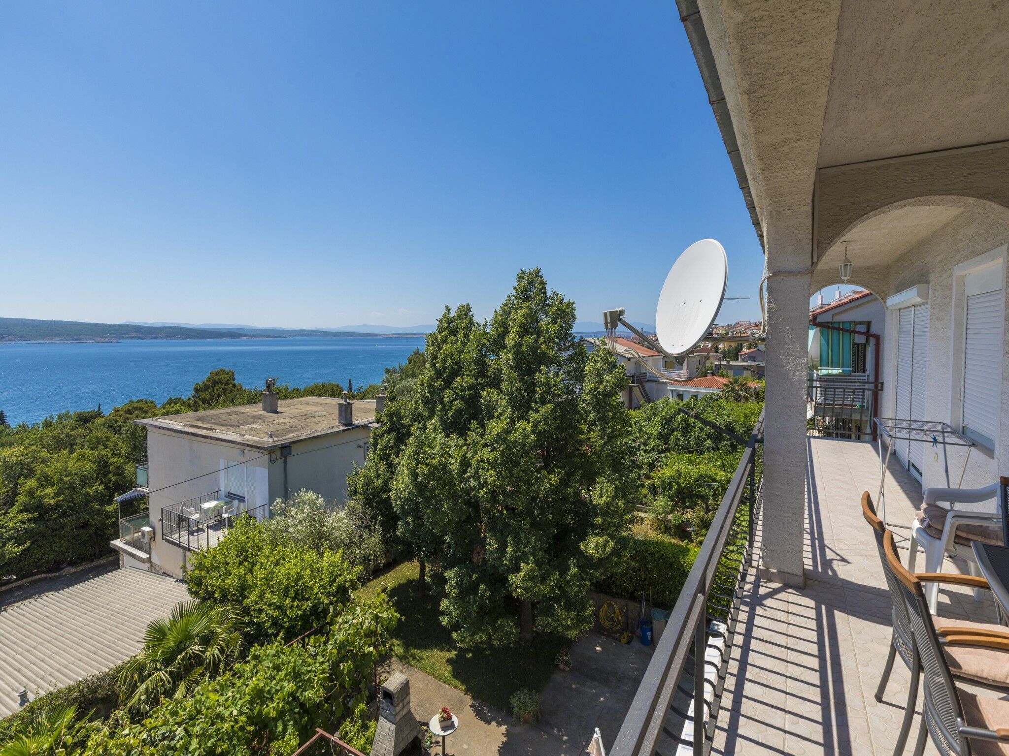 En balkon med udsigt over havet, en parabolantenne og en have.