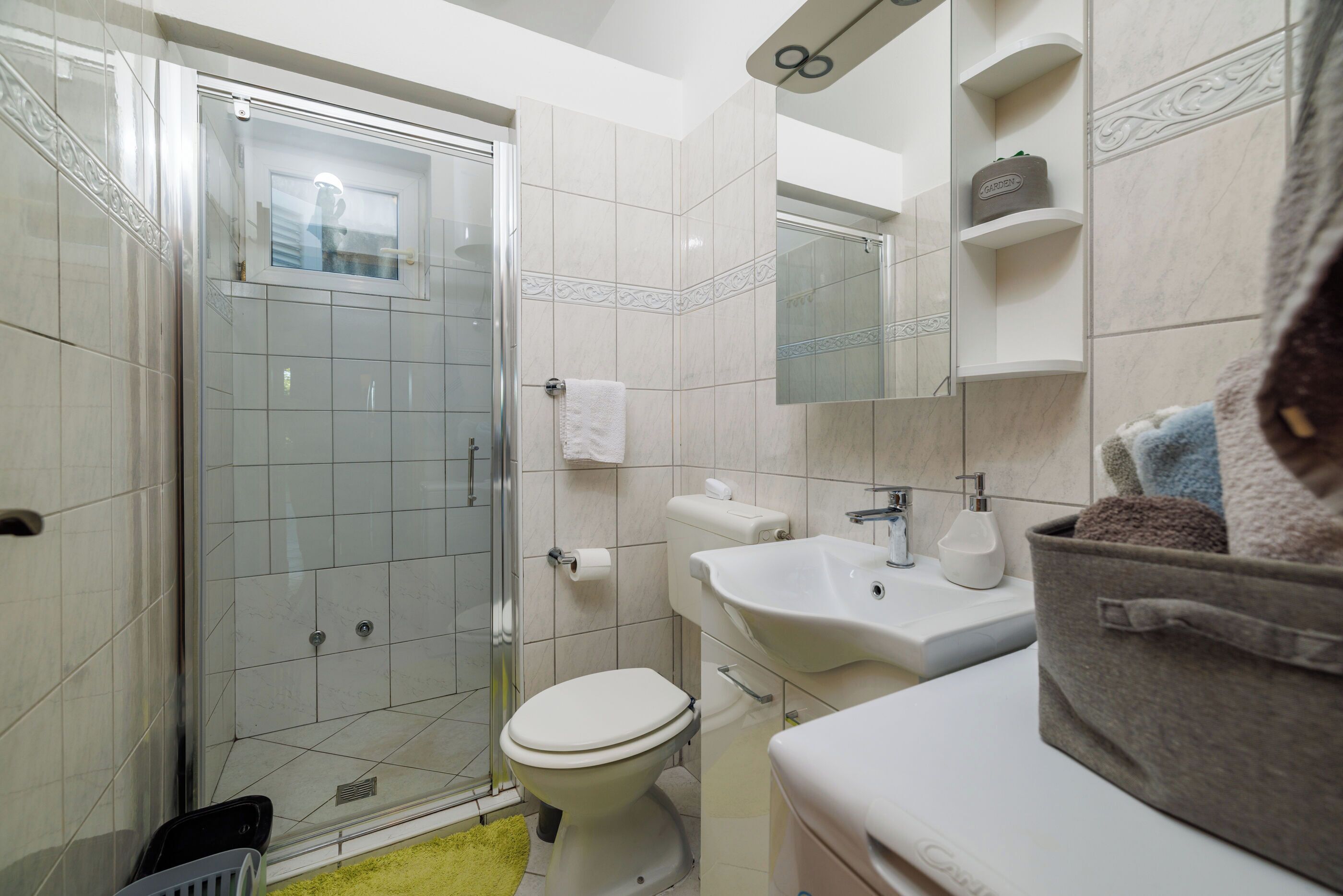A bathroom with a glass-enclosed shower, a toilet, a sink, and a mirror.