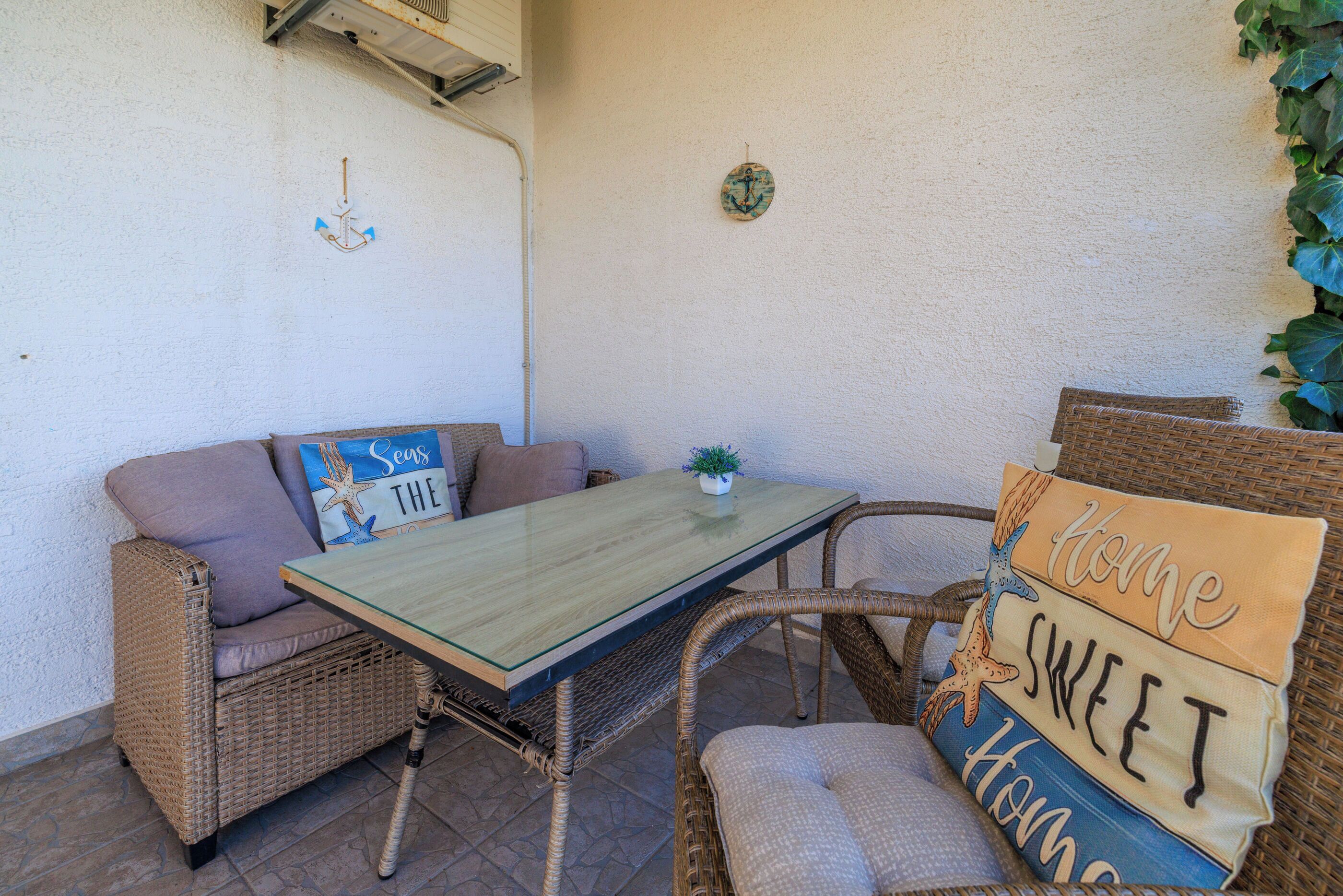 A wicker sofa and chair set with a glass-top table, a small potted plant, and decorative pillows with text.