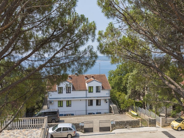 Un edificio de dos pisos con tejado de tejas, rodeado de árboles y con vista al mar.
