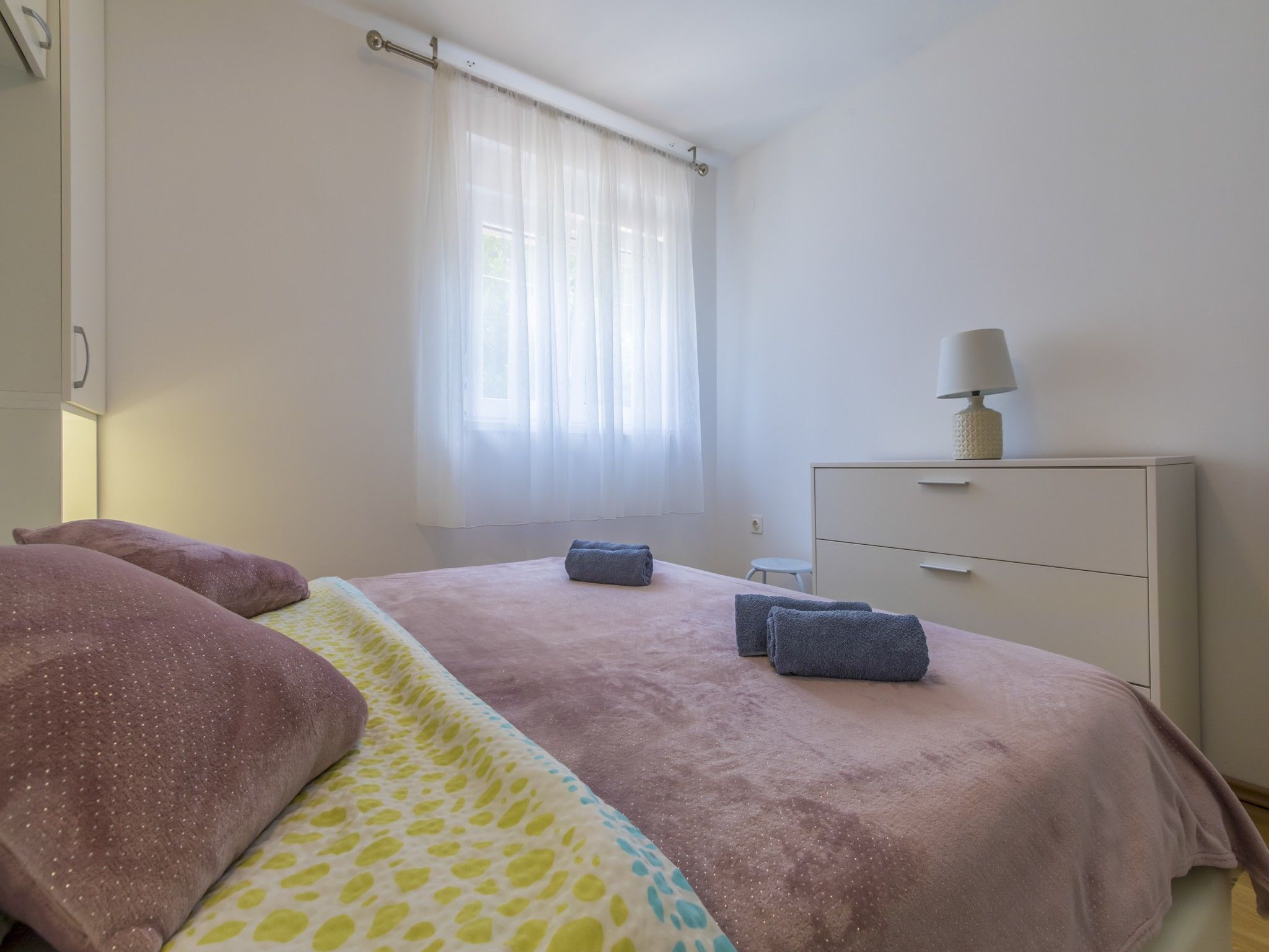 Un dormitorio con cama, mesita de noche, cómoda y ventana con cortinas.