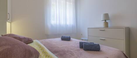 Un dormitorio con cama, mesita de noche, cómoda y ventana con cortinas.