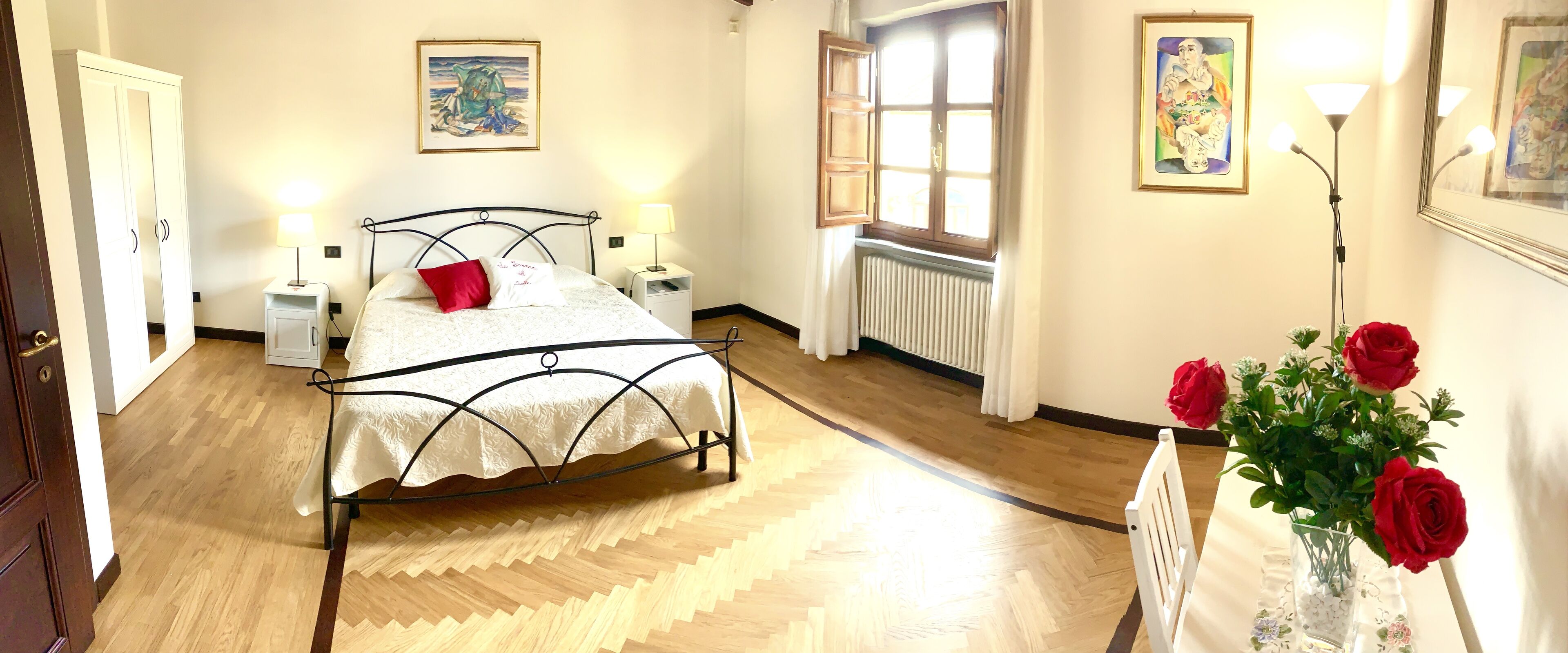 Une chambre à coucher avec un lit, des tables de chevet, une fenêtre et un vase rempli de fleurs.