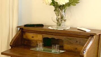 A wooden desk with a glass top, a vase with white flowers, and a green plant on the floor.