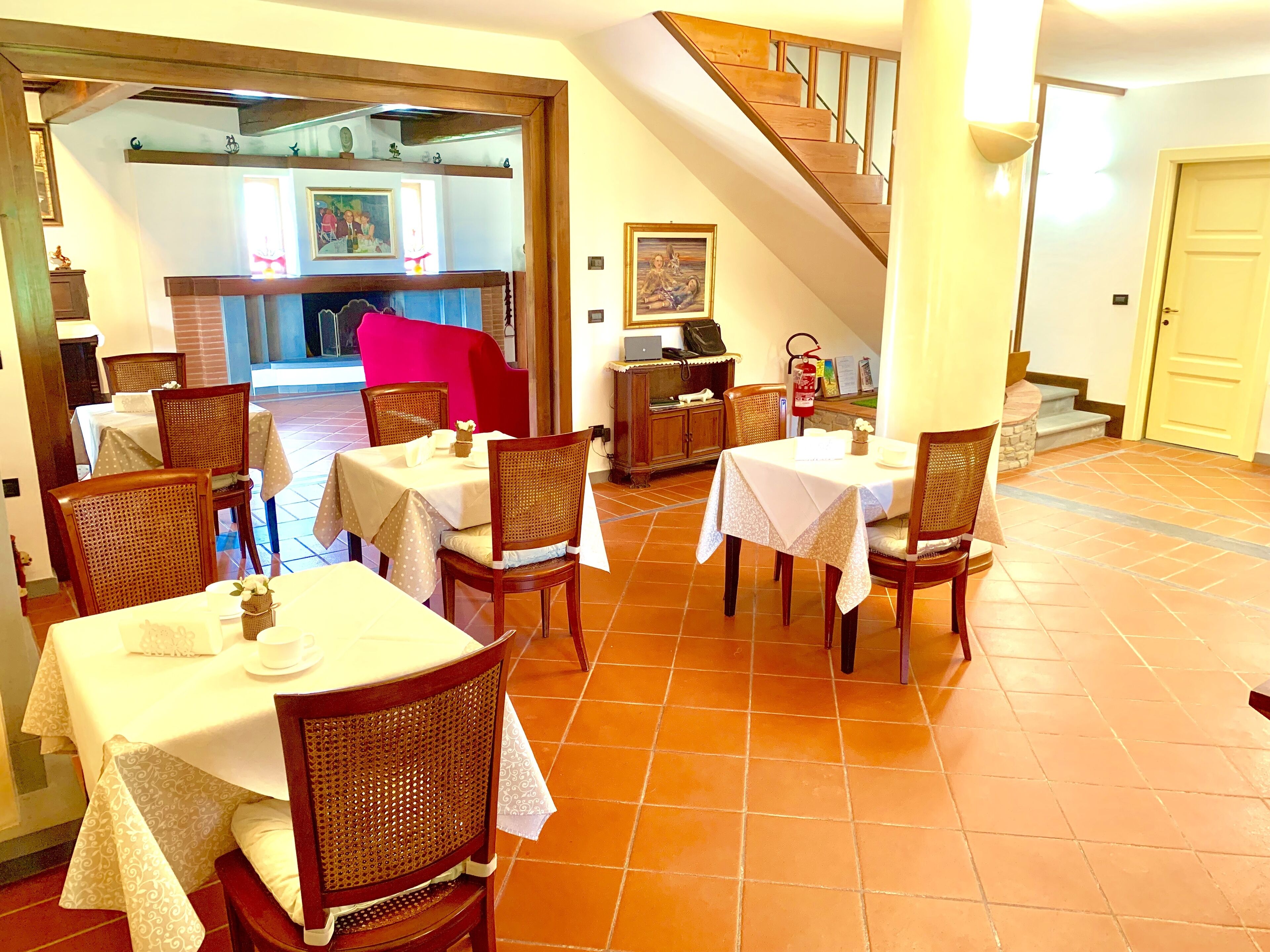 A dining area with tables and chairs, a staircase, and a kitchen area in the background.