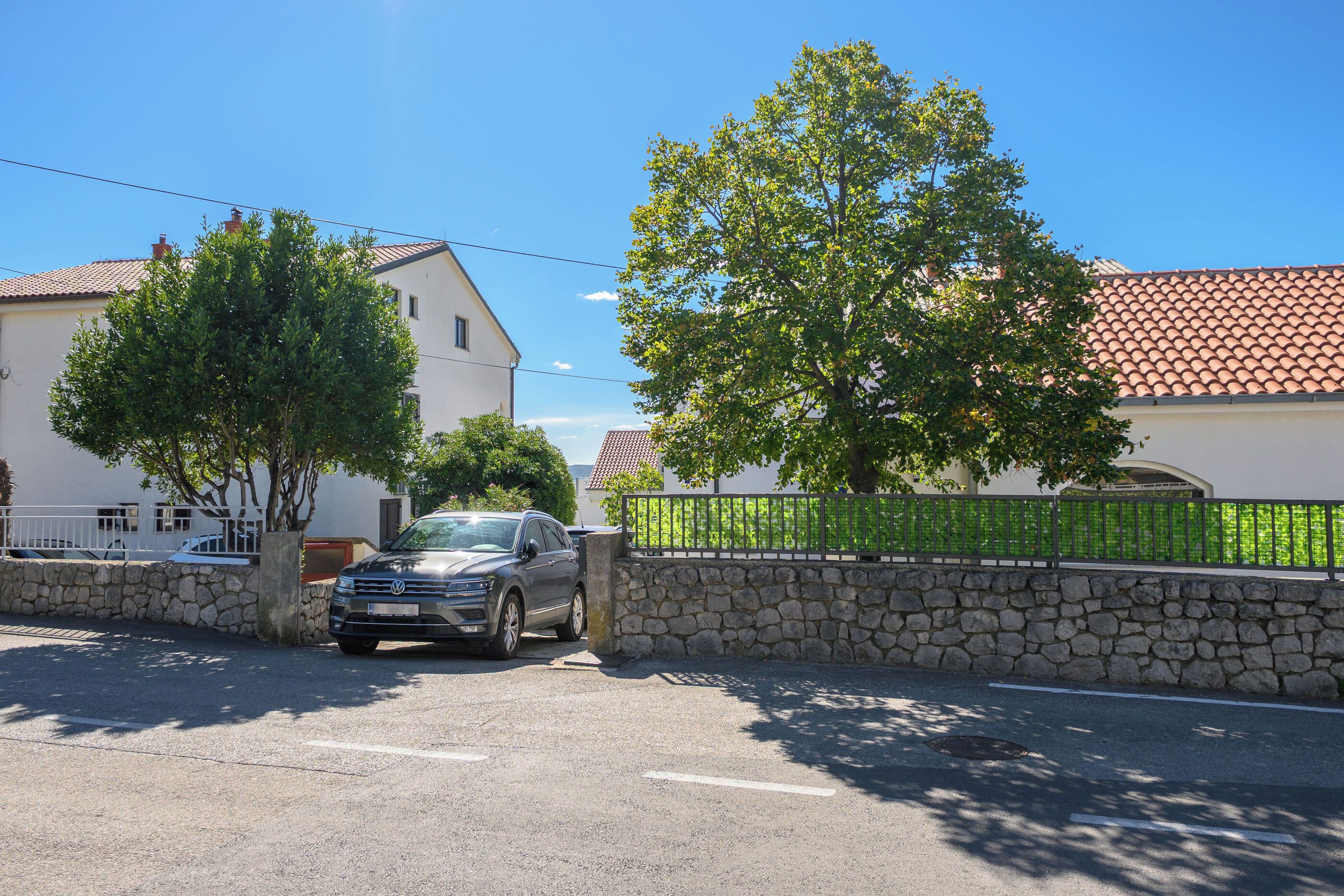 Una calle residencial con un coche aparcado, un muro de piedra y casas con tejados de tejas.