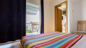 A hotel room with a bed, a wooden chair, and a view of a balcony and building outside. - Apartments Brankica (Dramalj)